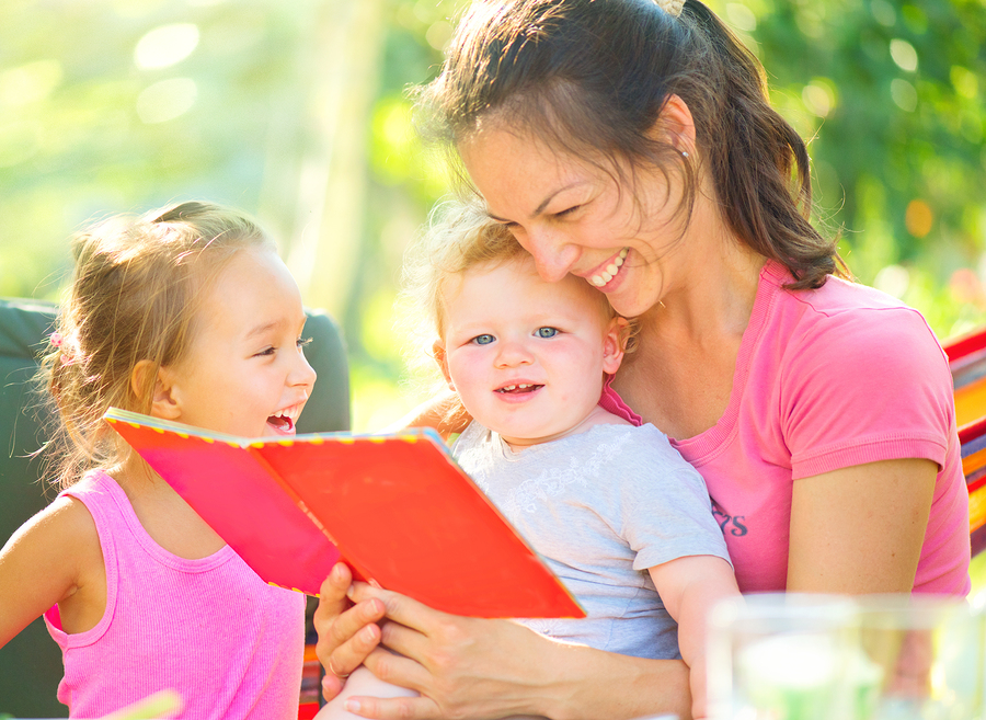 Happy mother reading a book to her little babies in sunny park.